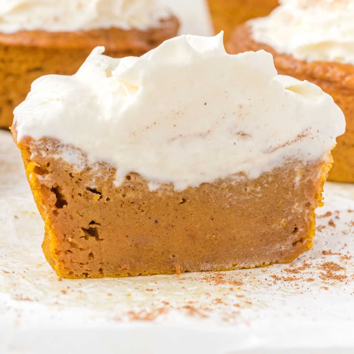 Pumpkin pie cupcake sliced open with whipped cream on top, sprinkled with cinnamon.