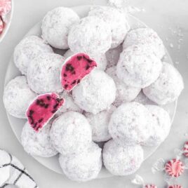 close up overhead shot of a plate of Peppermint Snowball Cookies with bowls of peppermint and chocolate chips