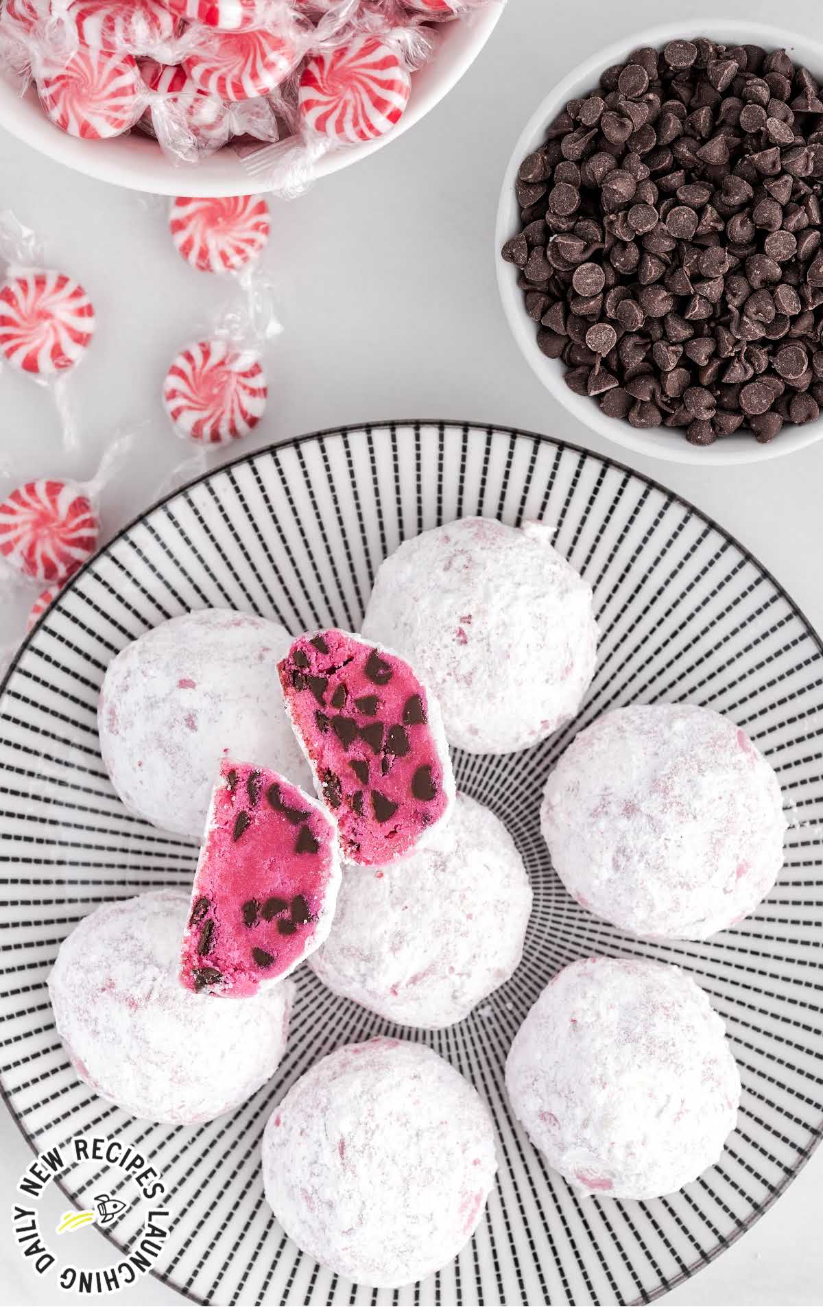 a plate of Peppermint Snowball Cookies with bowls of peppermint and chocolate chips