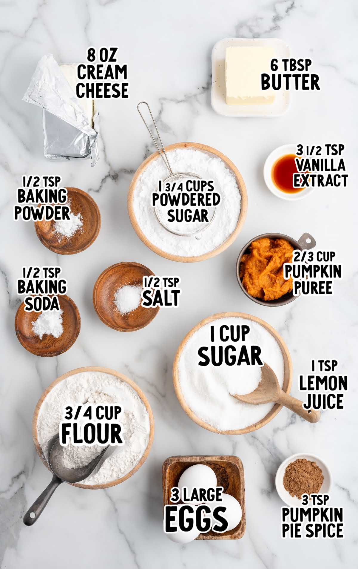 Measured ingredients for pumpkin roll laid out on marble surface including cream cheese, pumpkin puree, flour, sugar, and spices.