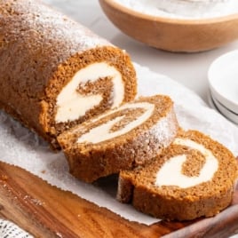 Pumpkin roll with cream cheese filling sliced and served on a wooden cutting board.