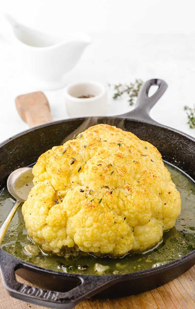 close up shot of the head of a Roasted Cauliflower topped with thyme in a skillet with a spoon