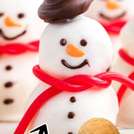 A decorated snowman truffle with a chocolate hat, red scarf, and smiling face. Other truffles are in the background. A step showing two stacked balls is at the bottom. Text reads: Snowmen Truffles Recipe. Easy to make!.
