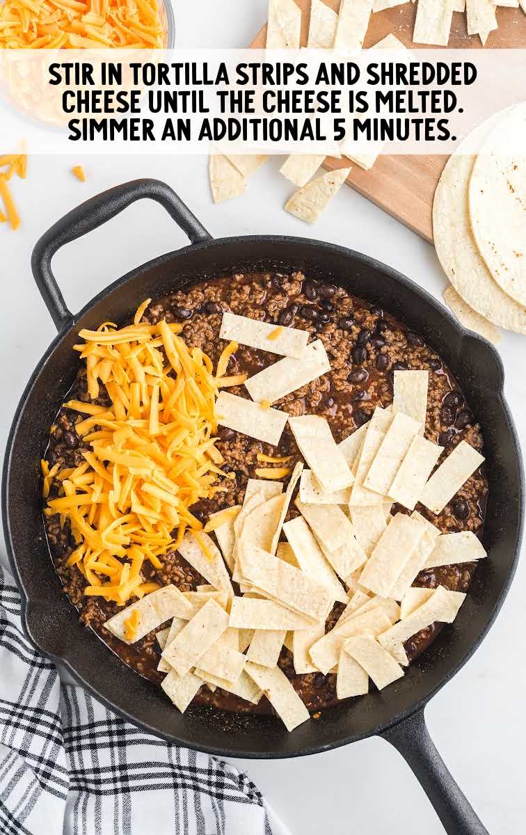 tortilla chips and shredded cheese added to the ground beef mixture in a skillet