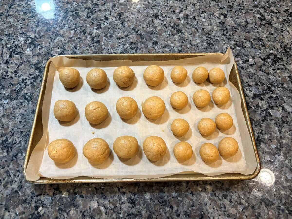 A baking tray lined with parchment paper holds 21 evenly spaced, round dough balls, arranged in rows, on a granite countertop—perfectly prepped as the first step for a delightful Snowmen Truffles Recipe.