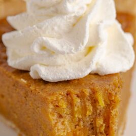 close up shot of a slice of Sweet potato pie topped with whipped cream on a plate