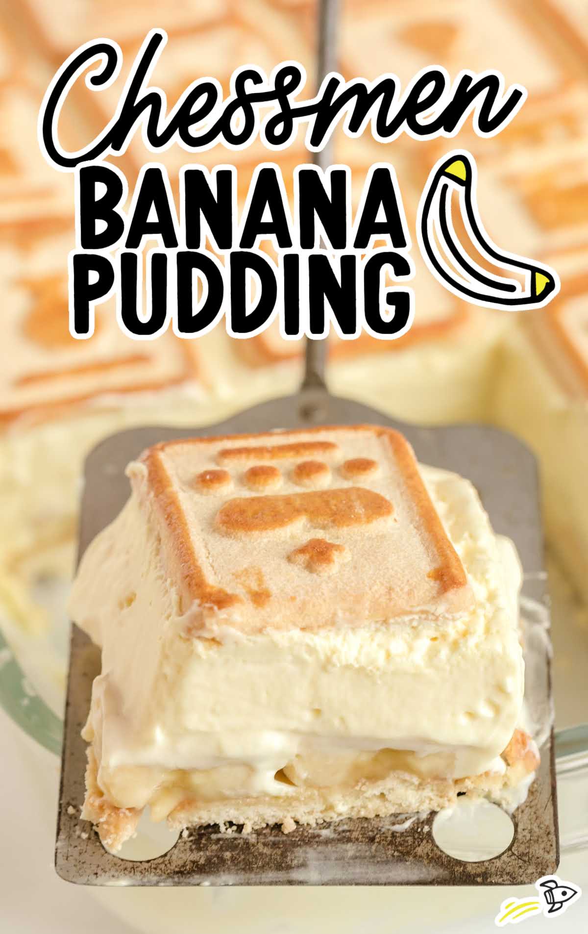 Slice of chessmen banana pudding being lifted from a dish, showing thick creamy layers and a chessmen cookie on top.

