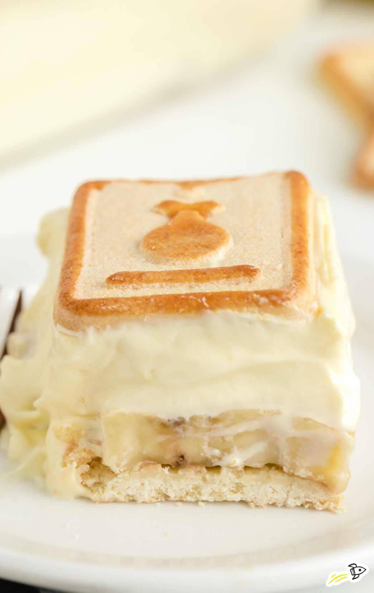 Side view of a square slice of chessmen banana pudding on a plate, highlighting the creamy filling and cookie base.
