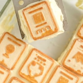 Overhead view of a square slice of chessmen banana pudding on a metal spatula above a baking dish.