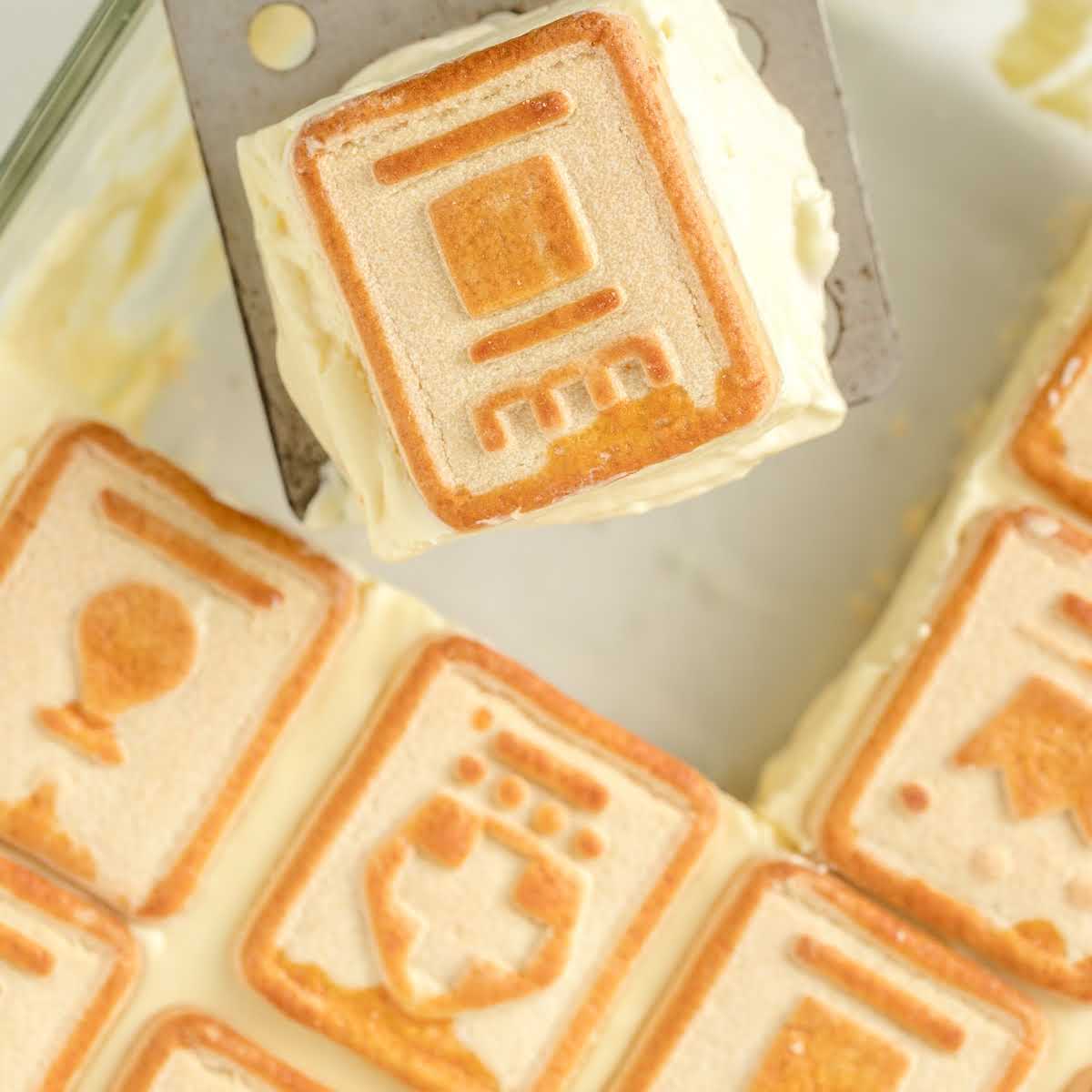 Overhead view of a square slice of chessmen banana pudding on a metal spatula above a baking dish.