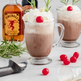 close up shot of glasses of drunken Rudolf topped with whipped cream and garnished with a maraschino cherry and rosemary