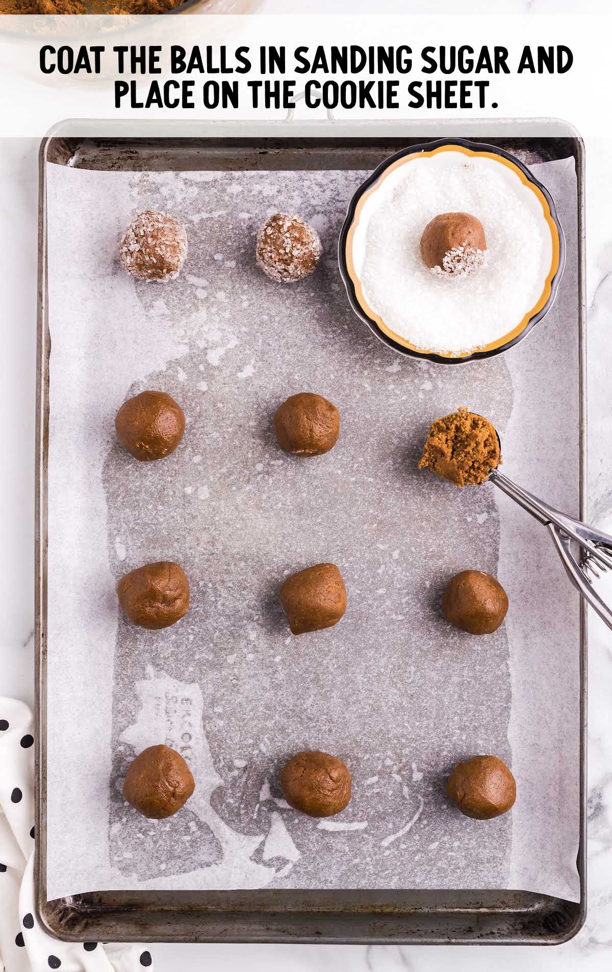 cookie dough balls being rolled into sanding sugar and placed on a cookie sheet