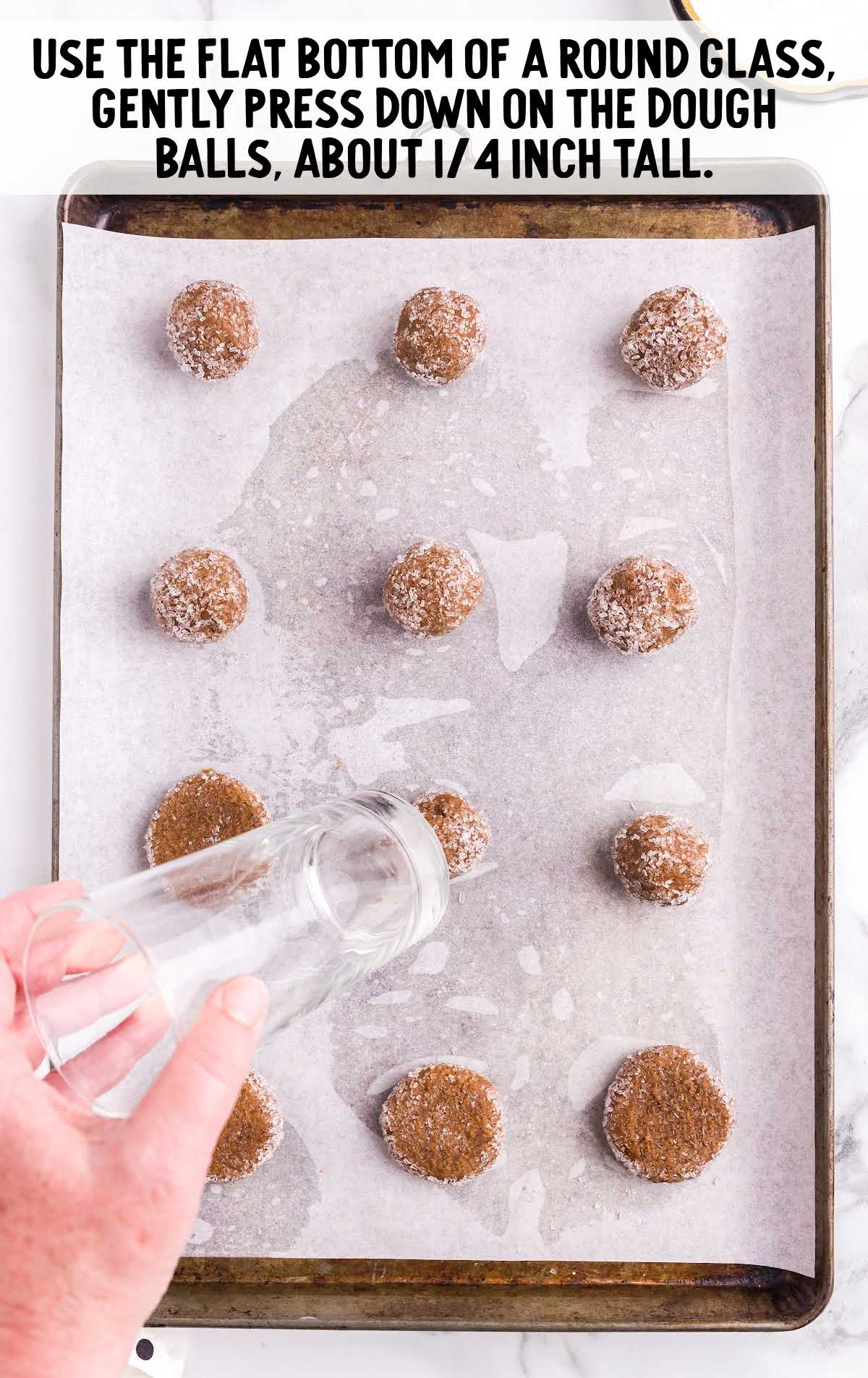 cookie dough balls being flattened with a glass on a cookie sheet