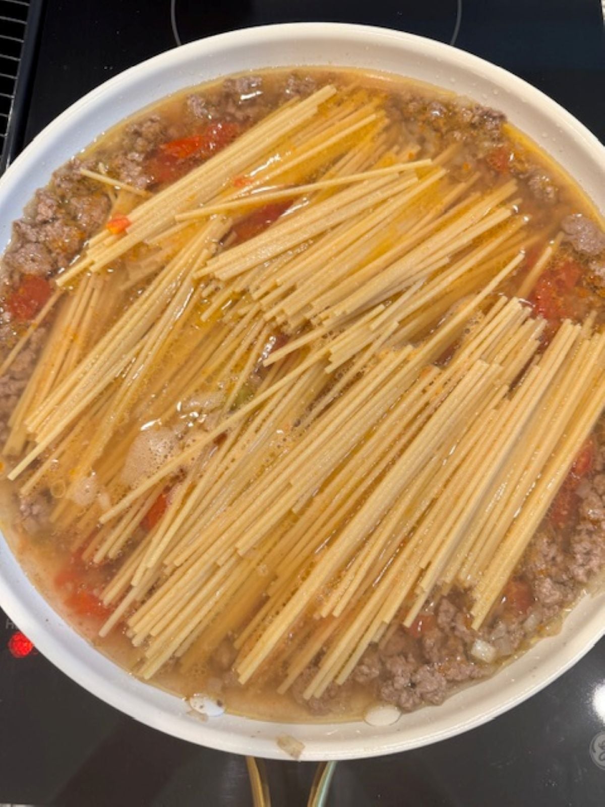 Uncooked spaghetti noodles simmer with ground beef, diced tomatoes, and broth in a pan to create a flavorful Taco Spaghetti recipe right on your stovetop.