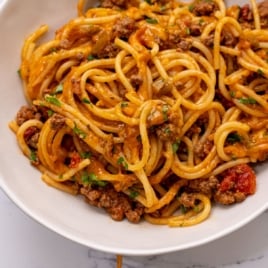 A close-up of a plate of Taco Spaghetti topped with a savory meat sauce, containing ground beef, diced tomatoes, and herbs, garnished with chopped parsley.