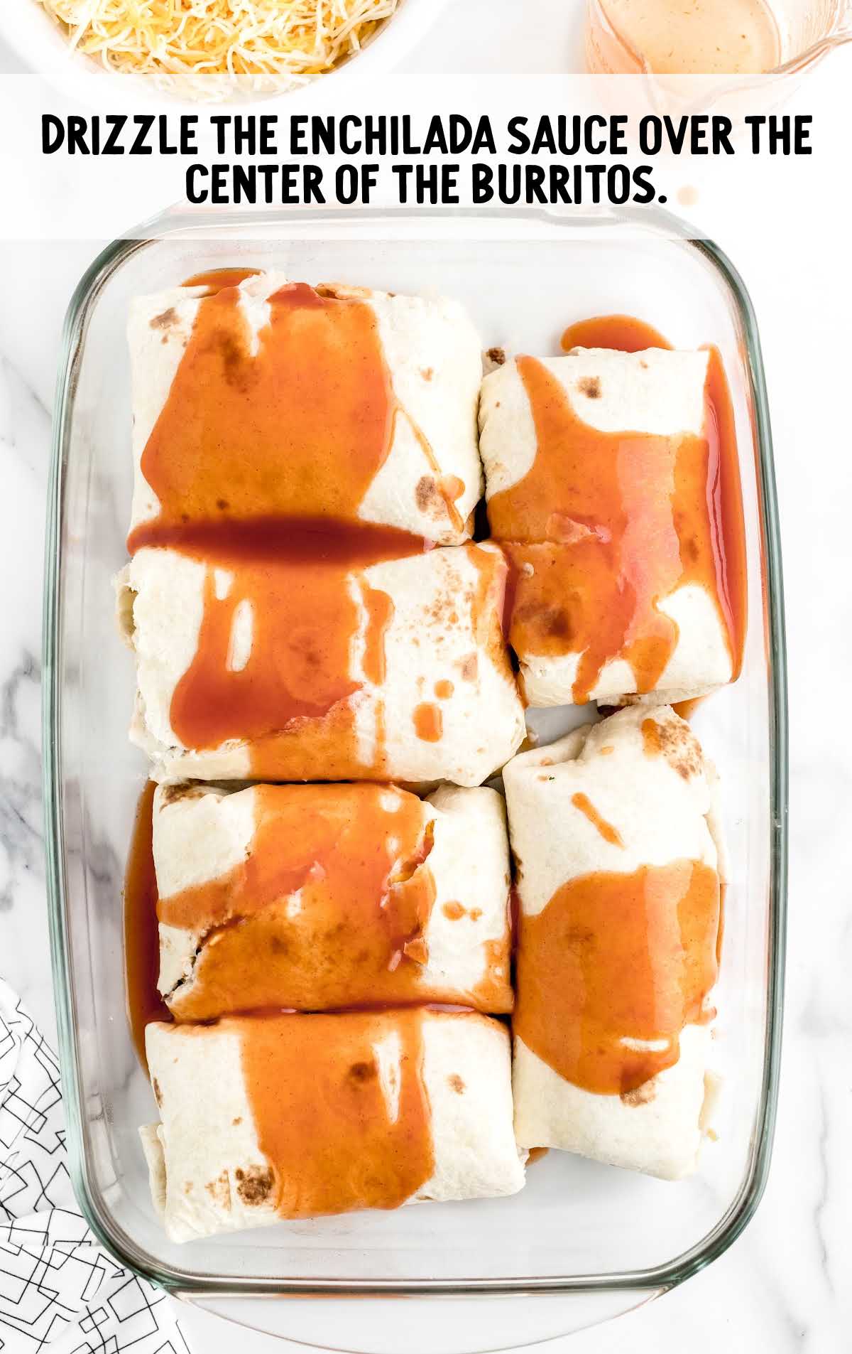enchilada sauce drizzled on top of burritos in a baking dish