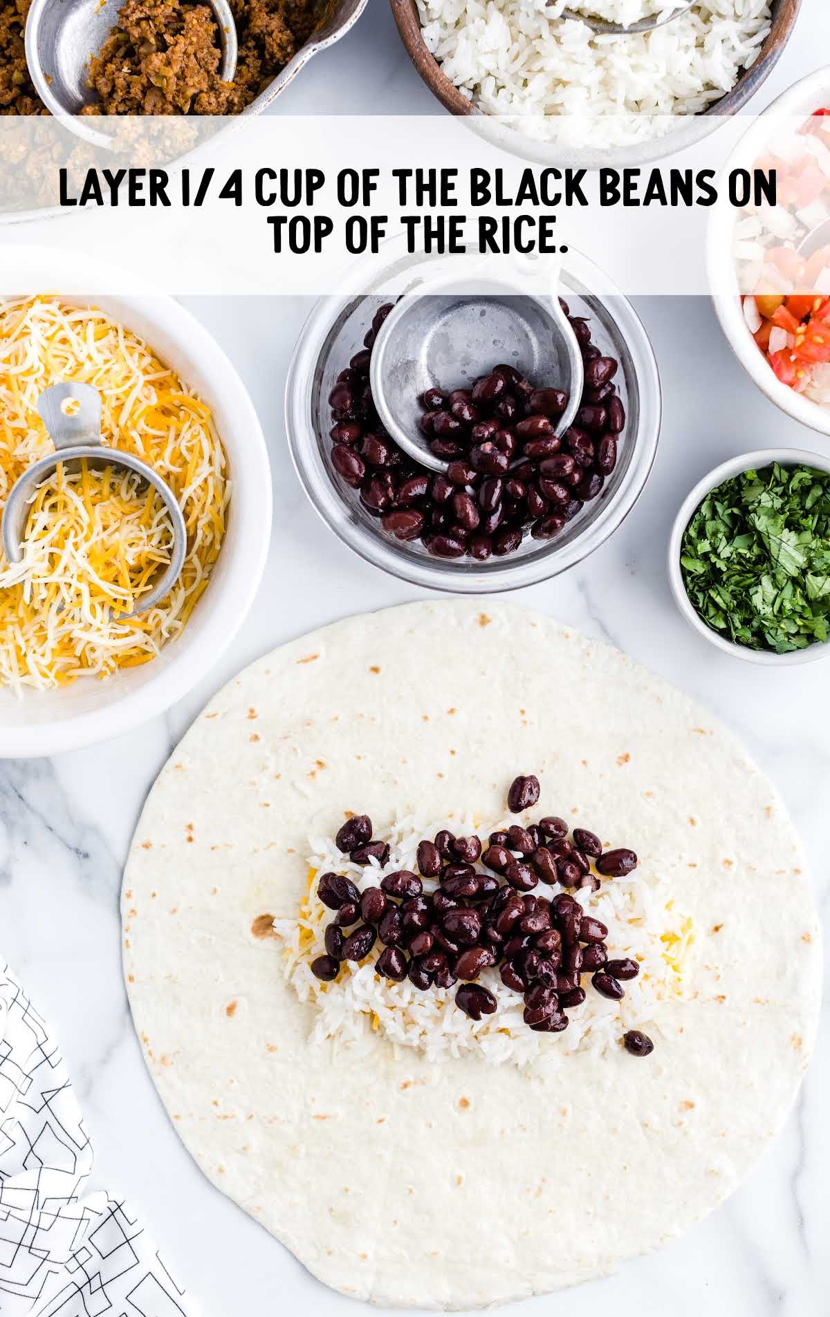 black beans being placed on top of the white rice on the tortilla