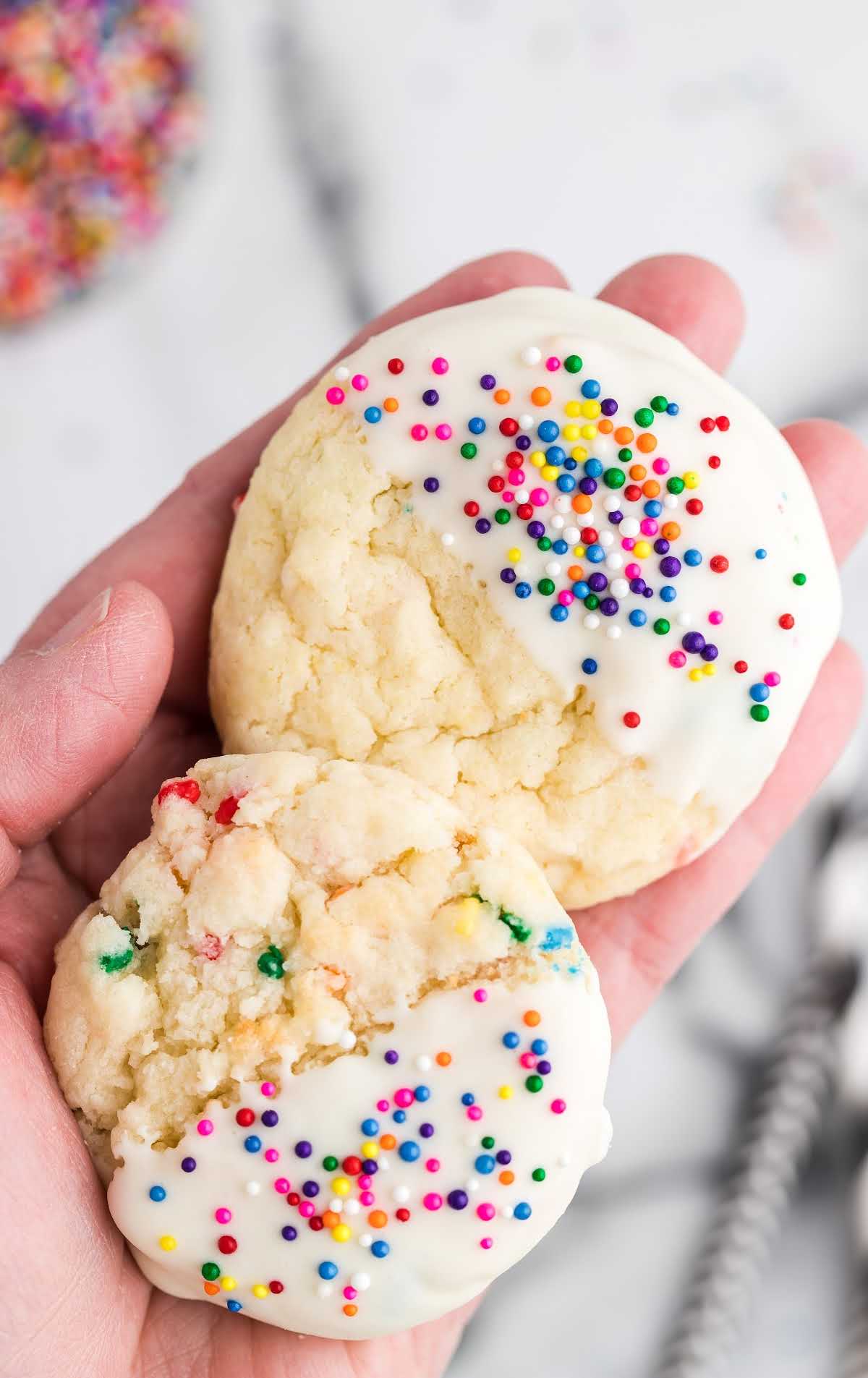 close up shot of a handful of cake mix cookies dipped in melted frosting and topped with sprinkles