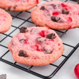 close up shot of Cherry Chocolate Chip Cookies on a cooling rack with a bowl of chocolate chips on the side