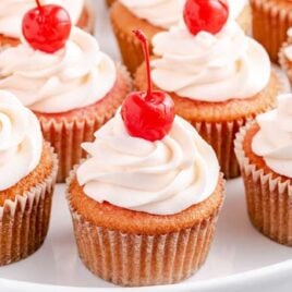 close up shot of a bunch of Cherry Cupcakes topped with frosting and a cherry on a serving tray