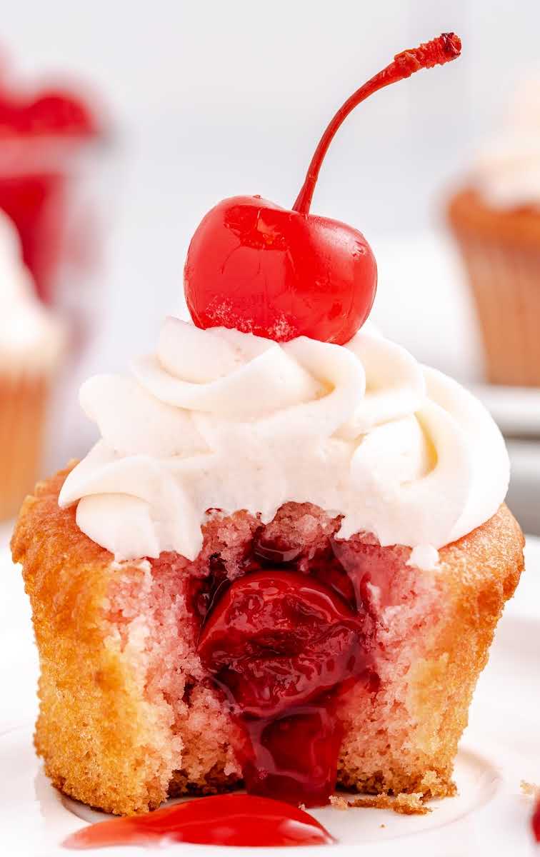 close up shot of a Cherry Cupcakes topped with frosting and a cherry on a plate