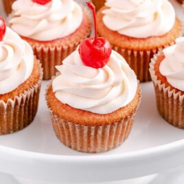 close up shot of a bunch of Cherry Cupcakes topped with frosting and a cherry on a serving tray