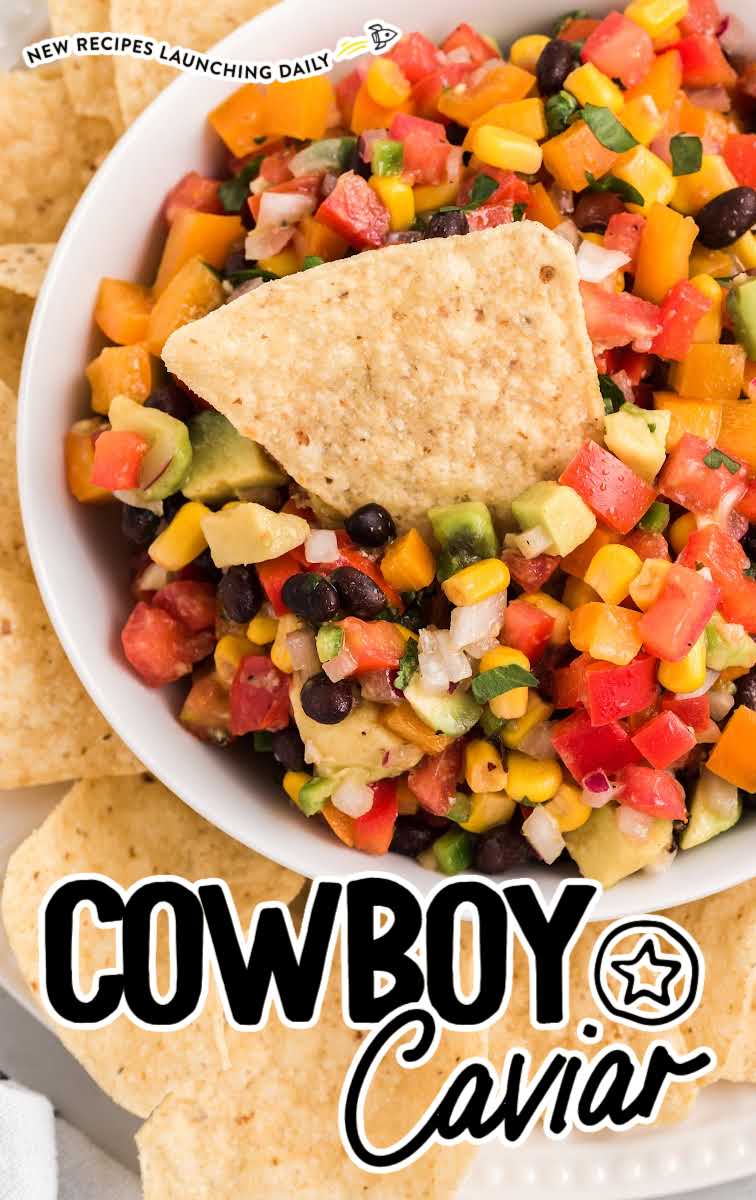 close up overhead shot of a bowl of Cowboy Caviar with a tortilla chip on top of a plate of tortilla chips