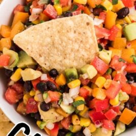 close up overhead shot of a bowl of Cowboy Caviar with a tortilla chip on top of a plate of tortilla chips