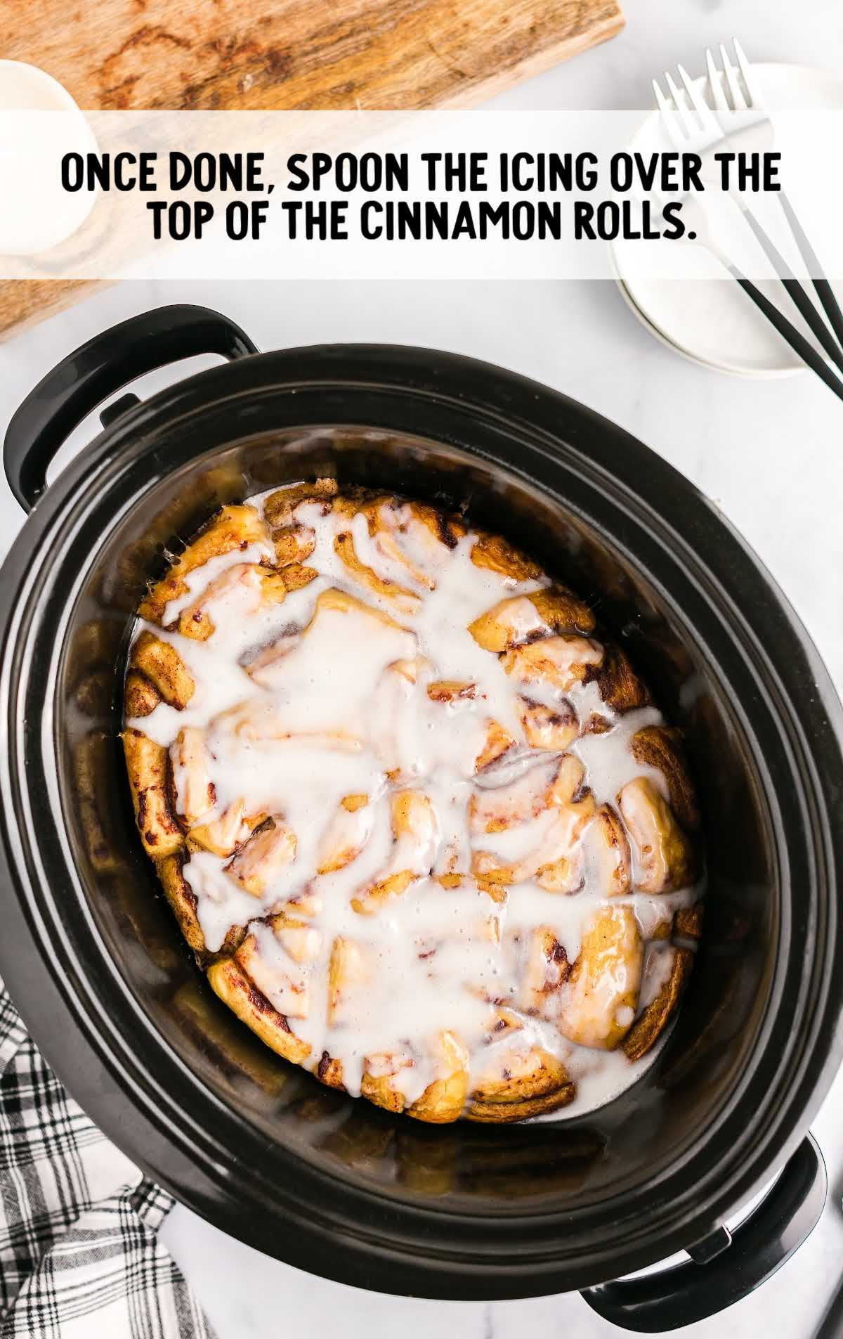 icing spooned on top of cinnamon rolls in a crockpot