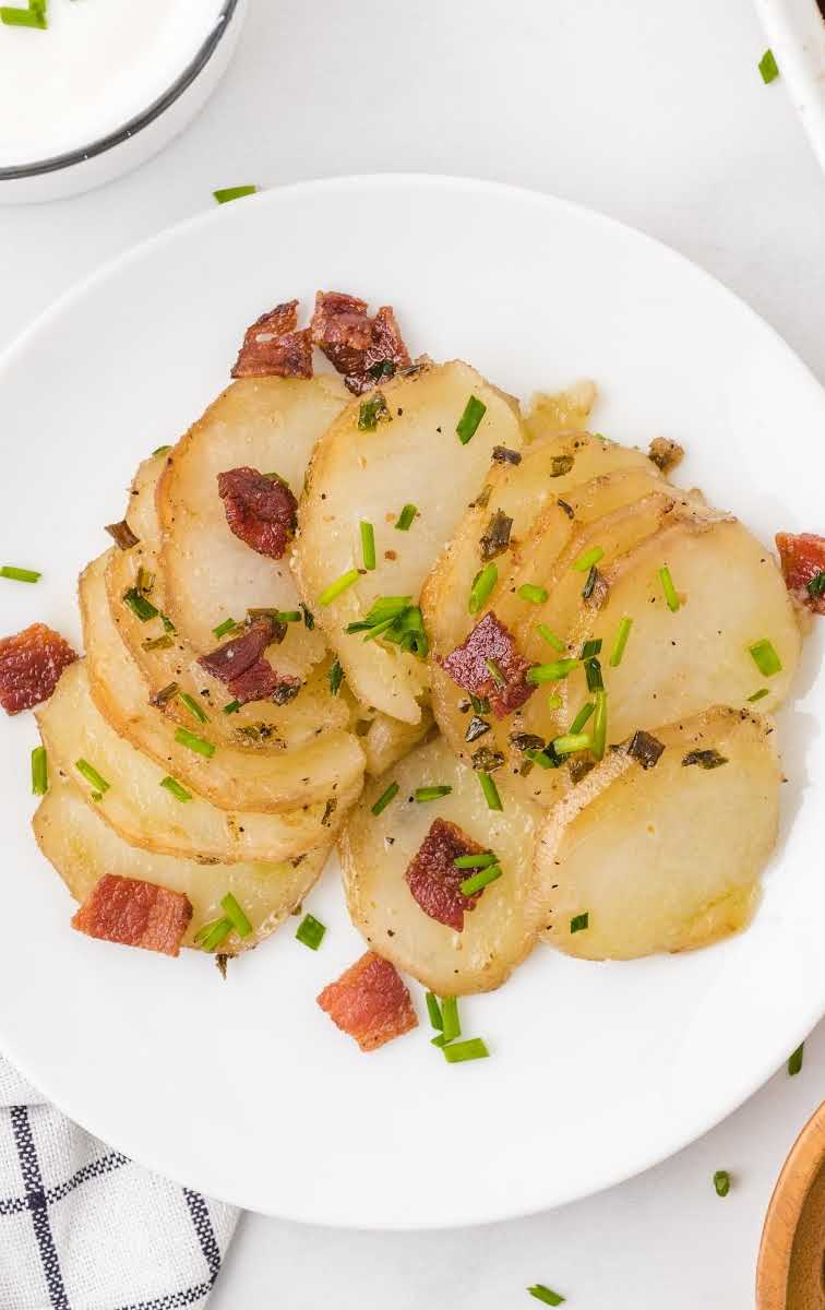 close up overhead shot of a serving of Hasselback Potato Casserole garnished with bacon bits and green onions on a plate