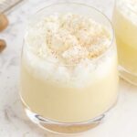 close up shot of a glass of Homemade Eggnog topped with whipped cream and sprinkled with cinnamon
