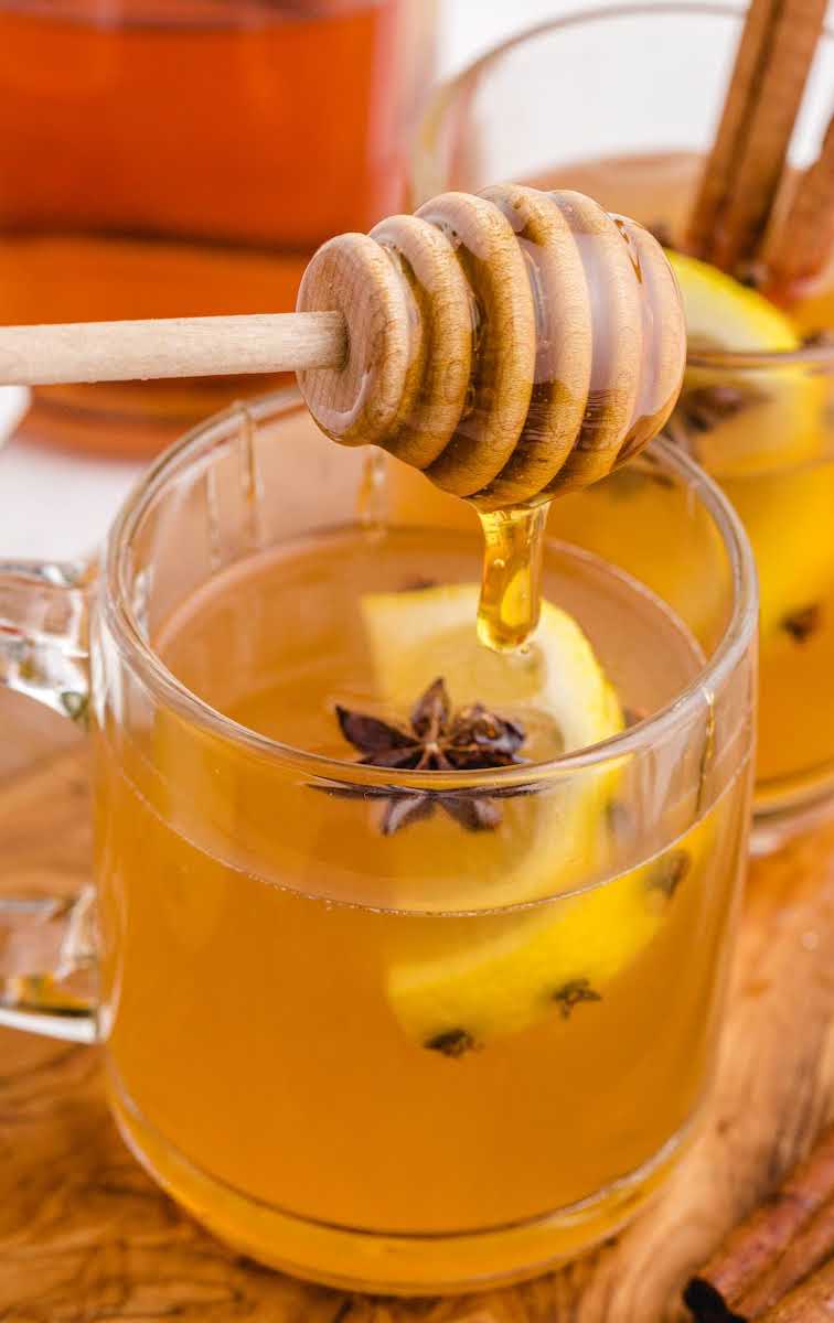 close up shot of a glass mug of Hot Toddy garnished with star anise and lemon with honey being added