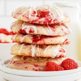 close up shot of Lemon Raspberry Cookies garnished with lemon glaze and stacked on a plate with raspberries
