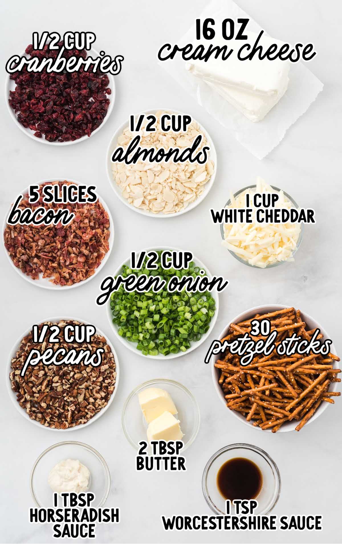 Flat lay of ingredients for mini cheeseball bites including cream cheese, bacon, cranberries, almonds, green onions, pecans, cheddar, pretzel sticks, butter, horseradish sauce, and Worcestershire sauce.