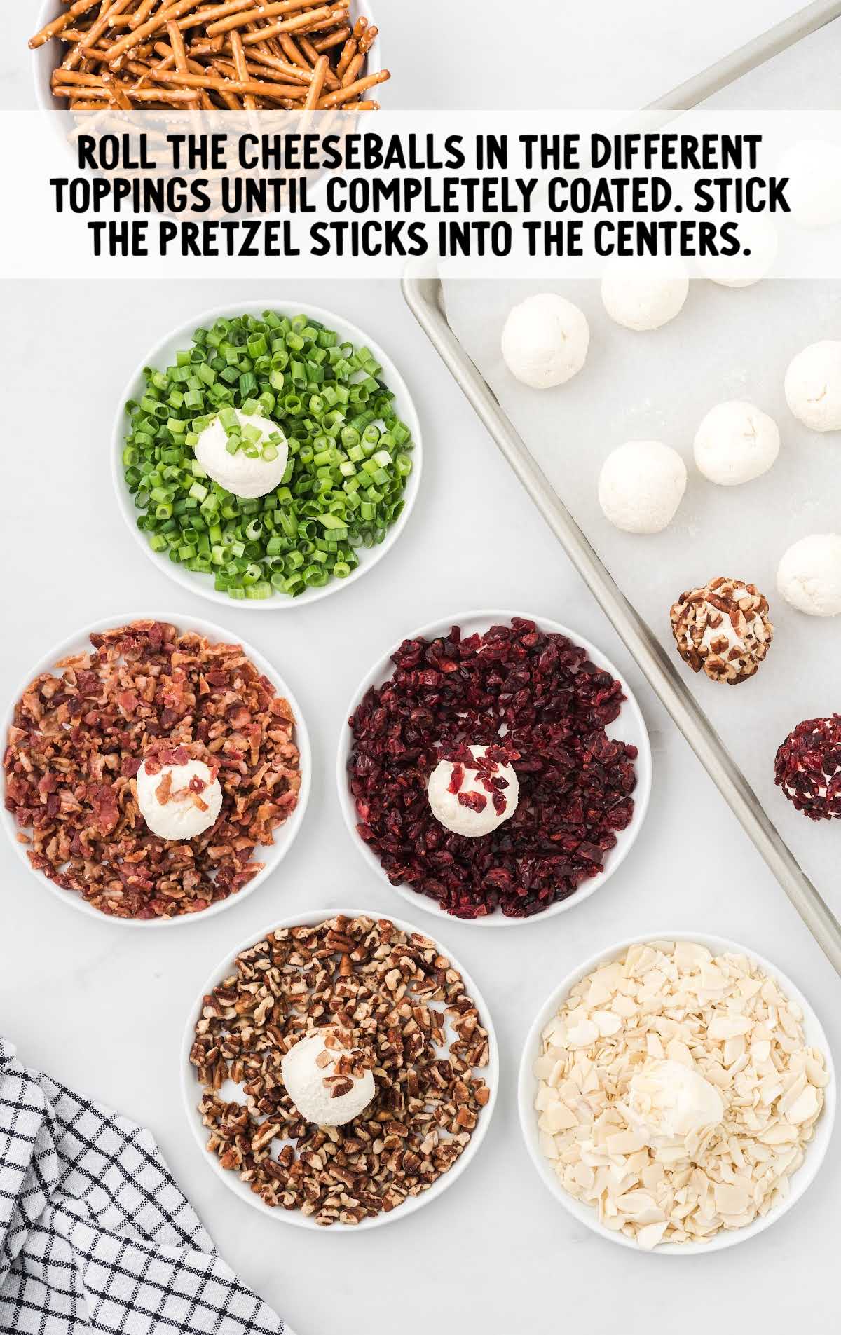 Cheeseballs being rolled in different topping bowls like green onion, pecans, bacon, cranberries, and almonds, with pretzel sticks ready to insert.