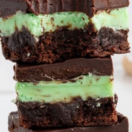 Three stacked mint chocolate brownies with a chocolate base, green mint layer, and chocolate topping. A bite is taken from the top brownie. Text reads Mint Chocolate Brownies Recipe and Vintage Recipe!.