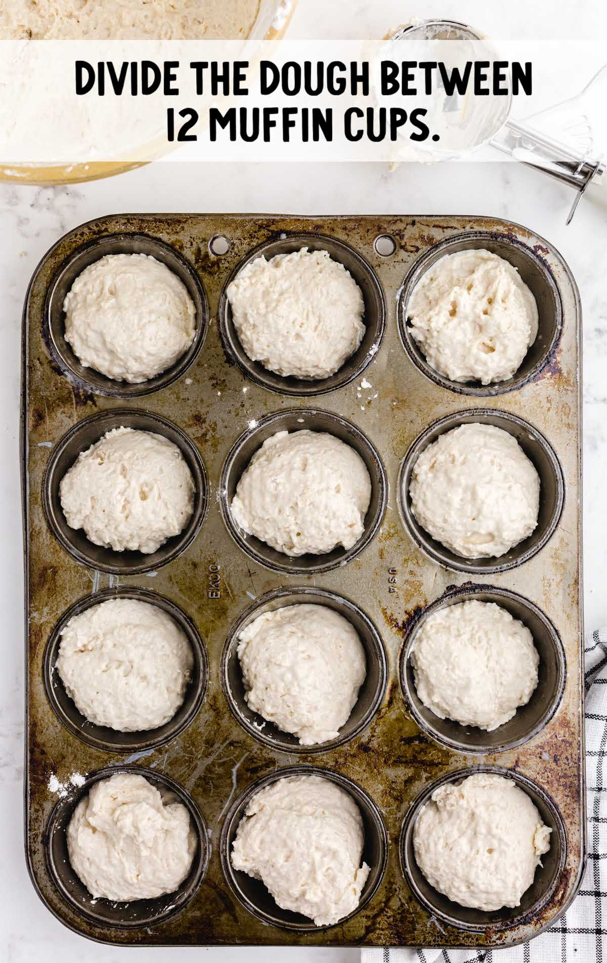 Overhead view of muffin pan filled with unbaked no yeast dinner roll dough divided into 12 cups.