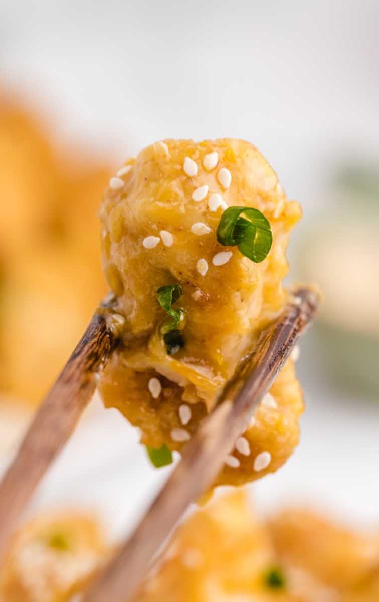 close up shot of Orange Chicken garnished with sesame seeds and green onions on chopsticks