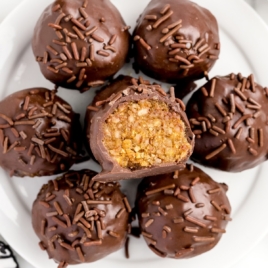 A white plate contains a bunch of pecan pie balls, and one is cut open to show the pecan pie filling.