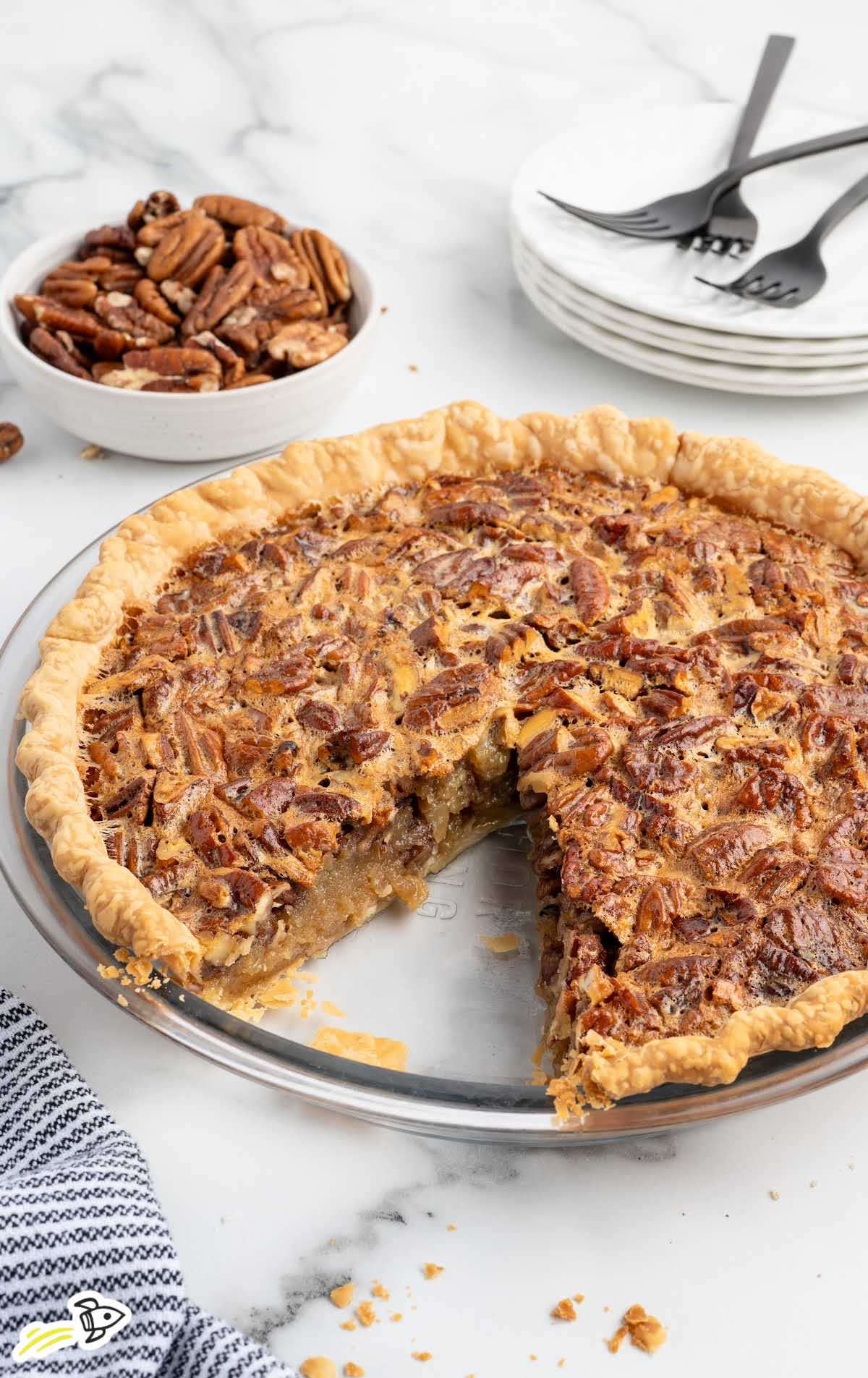 Whole baked pecan pie in a glass pie dish with a slice removed.