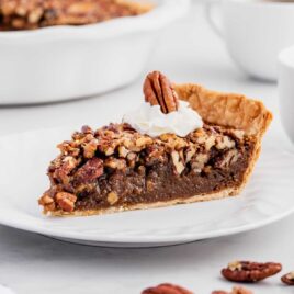 a slice of Pecan Pie topped with whipped cream and a pecan on a plate