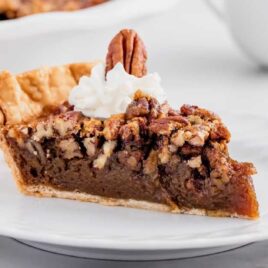 a slice of Pecan Pie topped with whipped cream and a pecan on a plate