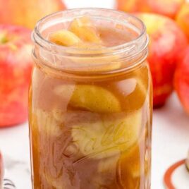 close up shot of a jar of apple pie filling with a bunch of apples in the back