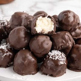 Chocolate coconut balls on a white plate, some topped with shredded coconut.