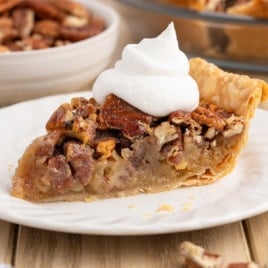 Slice of pecan pie topped with whipped cream on a white plate.