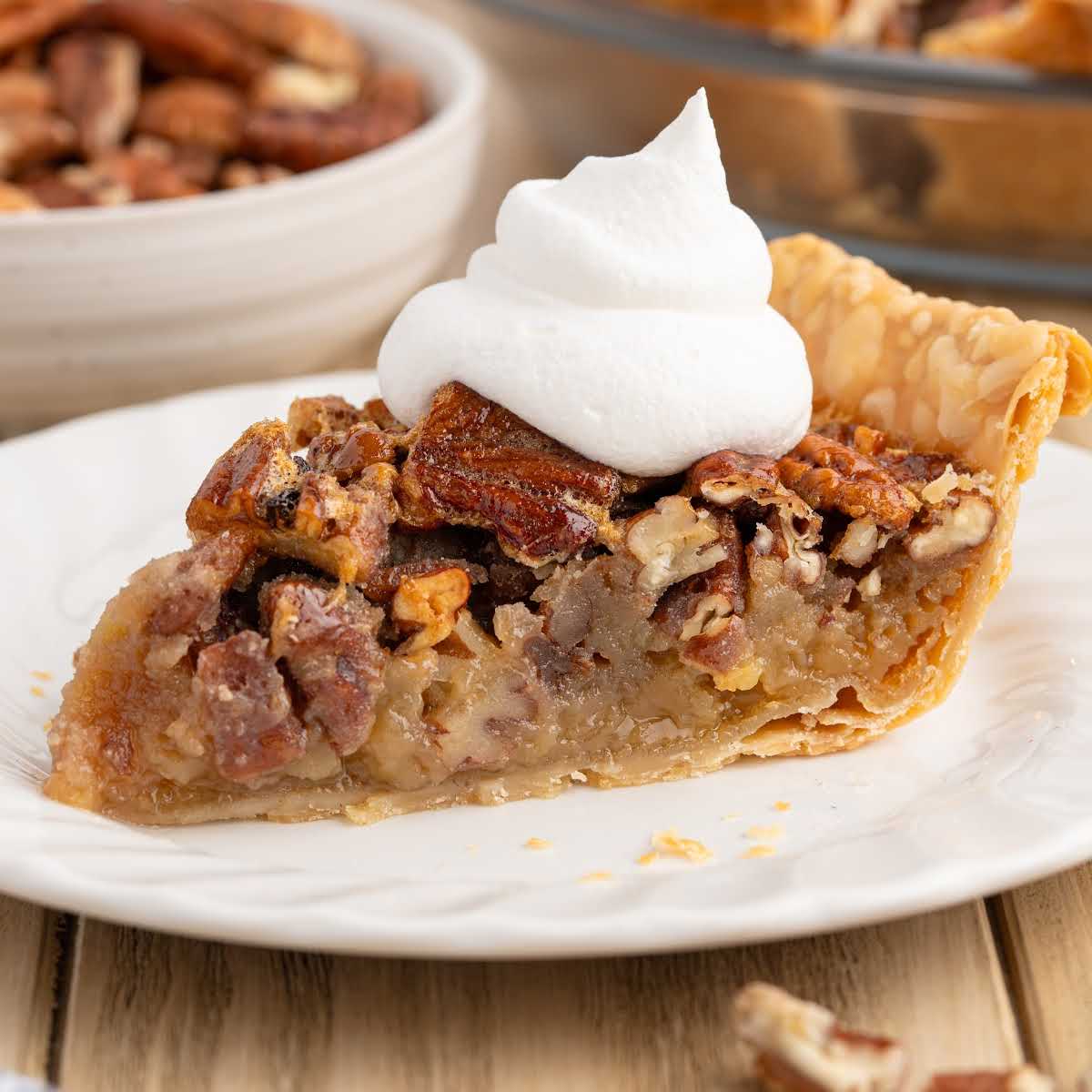 Slice of pecan pie topped with whipped cream on a white plate.