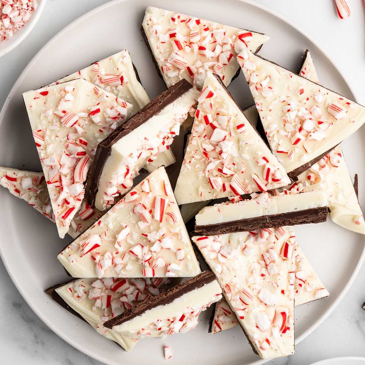 Plate of peppermint bark triangles made with layers of dark and white chocolate topped with crushed candy canes