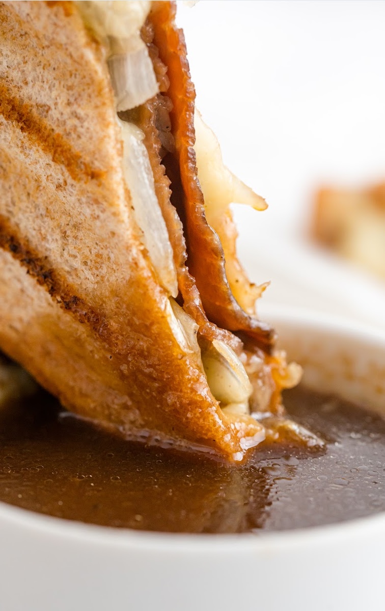close up shot of a slice of roast beef panini with au jus being dipped into a roast beef sauce