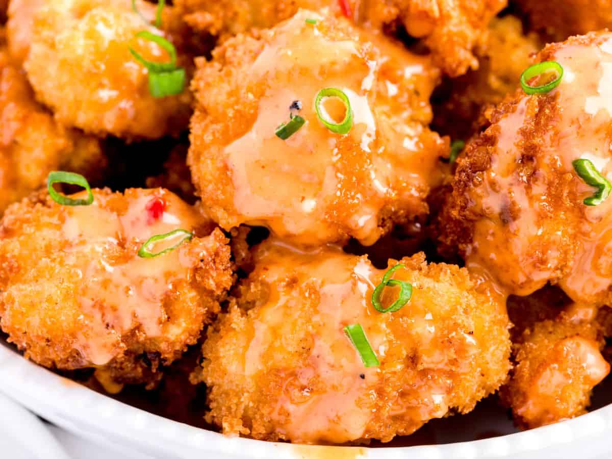 Crispy fried shrimp coated in a creamy orange sauce, reminiscent of the flavors found in a classic Bang Bang Chicken Recipe, garnished with sliced green onions and served in a white dish.