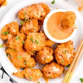 A plate of crispy fried shrimp topped with a tangy sauce and chopped green onions, served alongside a bowl of dipping sauce and a pair of wooden chopsticks on the side, drawing inspiration from the bold flavors found in the classic Bang Bang Chicken Recipe.